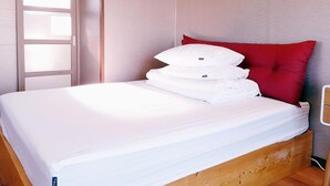 Een net opgemaakt bed met witte beddengoed en een rood kussen, een houten hoofdbord en een houten vloer.
