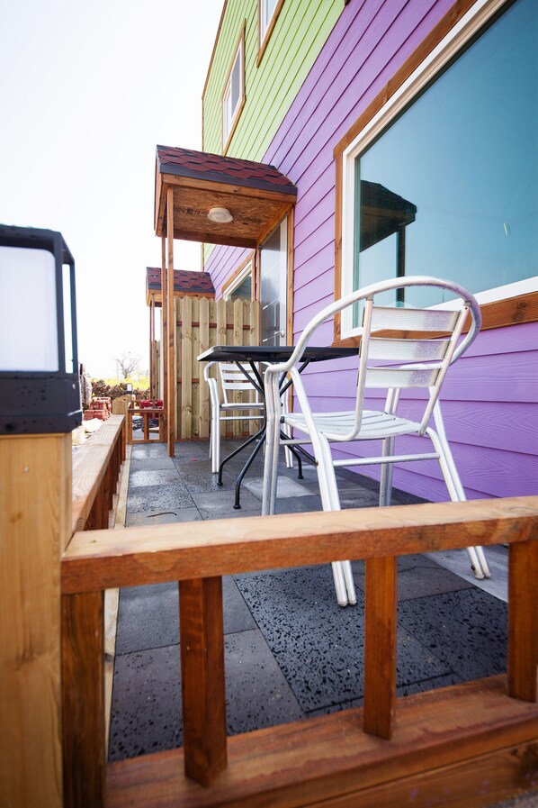 A patio with a wooden table and chairs, a wooden bench, and a wooden structure with a red roof.