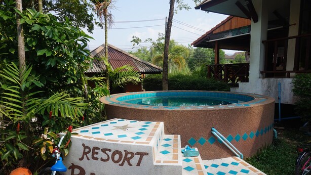 A swimming pool with a sign reading "RESORT BUPPHA" surrounded by greenery and a building in the background. - Buppha Resort (Takua Pa)