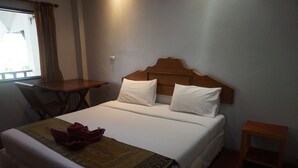 A neatly made bed with white linens and a brown headboard, a small wooden table, and a chair to the left. - Buppha Resort (Takua Pa)