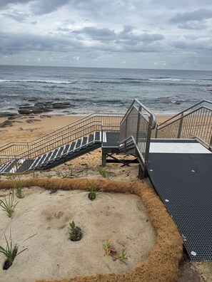 Ein Strand mit einer Metalltreppe, die zu einem Holzdeck mit Blick auf den Ozean führt.