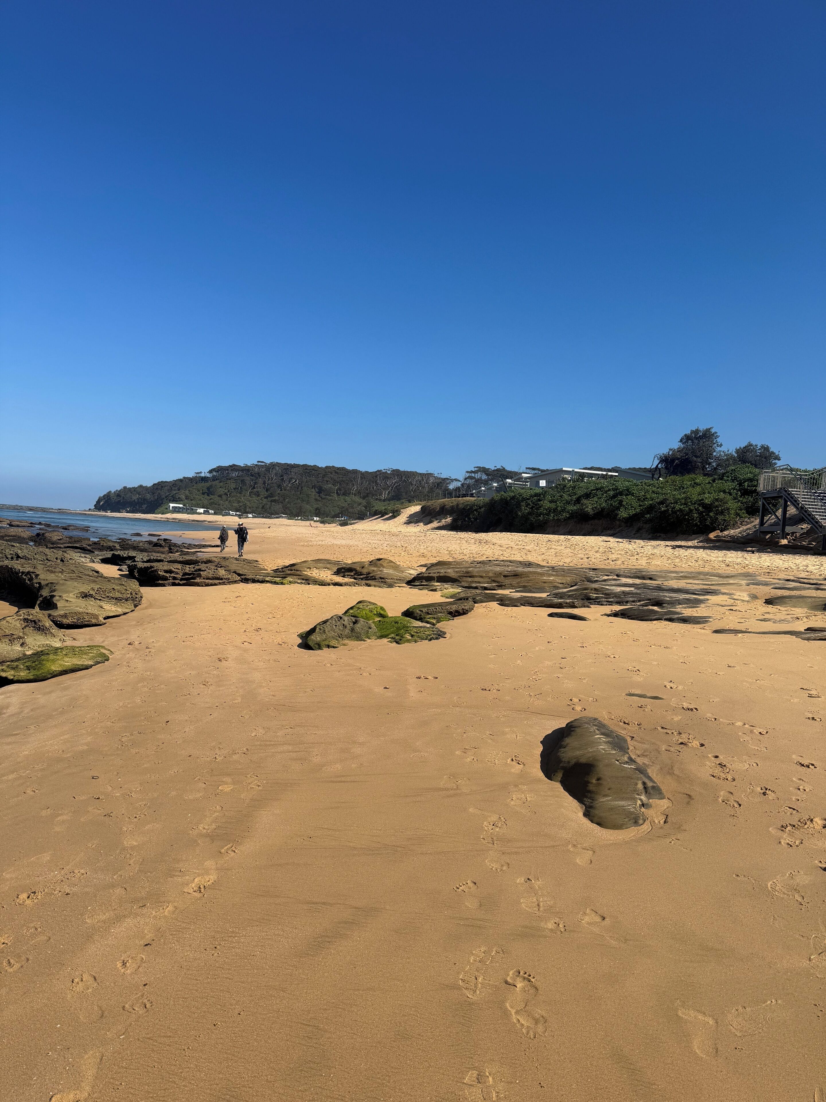 A sandy beach with footprints, a rocky outcrop, and a clear blue sky.