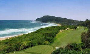 Un paisaje costero con un campo de golf, una playa y una colina arbolada.