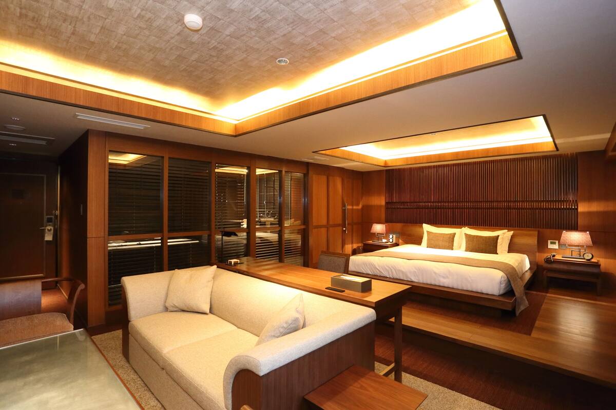 A modern hotel room with a wooden floor, a sofa, a bed, a desk, and a wardrobe.