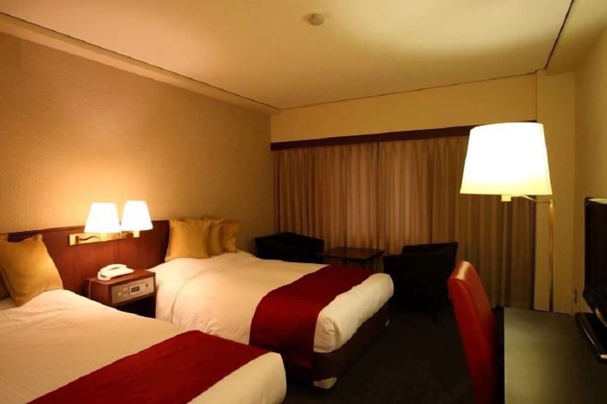 Una habitación de hotel con dos camas, un escritorio, una silla, un televisor y una lámpara.