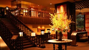 A lobby with a grand staircase, a round table with a vase of flowers, and a bookshelf. - Urban Villa Konaya Hotel (Kofu)