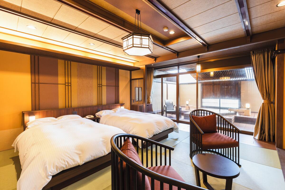 A hotel room with two beds, a sitting area with a chair and table, and a view through a large window.