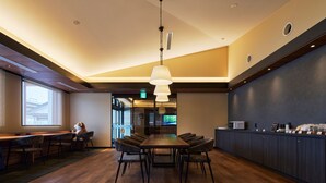 A modern hotel lobby with a long dining table, comfortable seating, a reception desk, and a large window providing a view. - ホテルB4T角館 (Senboku)
