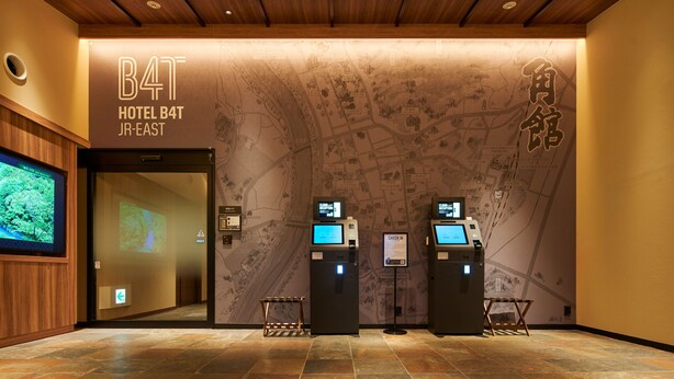 A hotel reception area with a wooden ceiling, a map mural, and two check-in kiosks. - ホテルB4T角館 (Senboku)