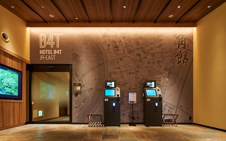 A hotel reception area with a wooden ceiling, a map mural, and two check-in kiosks.