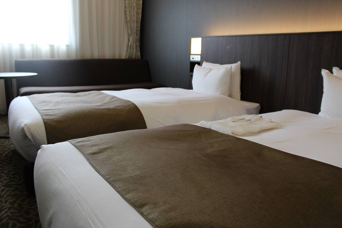 A hotel room with two beds, a small table, and a headboard with a light fixture.