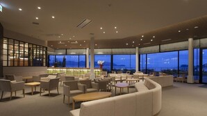 Un vaste espace salon doté de nombreux sièges, de grandes fenêtres offrant une vue sur l’extérieur et d’un bar avec des étagères.