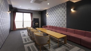 A conference room with a long table, chairs, a sofa, patterned wallpaper, and a window with curtains.