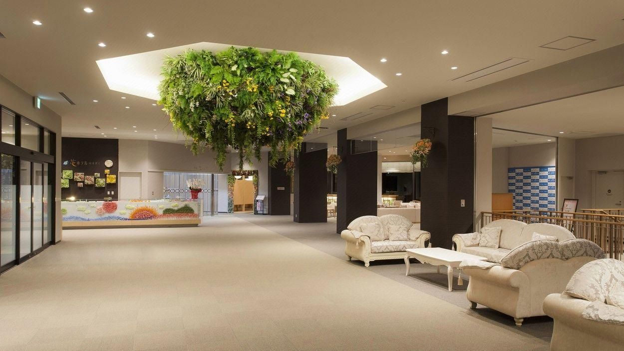 A spacious lobby with a central hanging plant, seating area, and a reception desk.