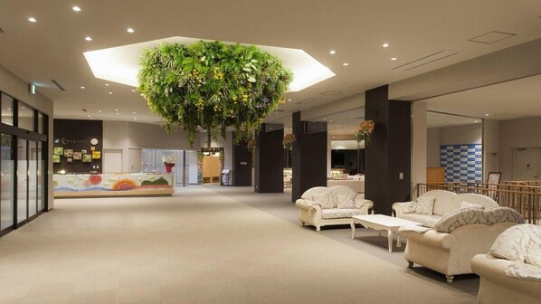 A spacious lobby with a central hanging plant, seating area, and a reception desk.