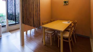 Uma área de refeições com mesa e cadeiras de madeira, uma janela com cortinas e uma pequena decoração floral na parede.