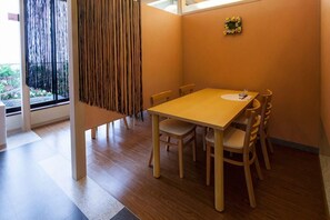 Un coin repas avec une table et des chaises en bois, une fenêtre avec des rideaux et une petite décoration florale au mur.