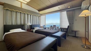 A hotel room with two beds, a desk, a chair, and a view of the sea.