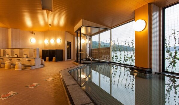 Een modern binnenzwembad met glazen barrière, een sauna met banken, en uitzicht op een meer door grote ramen.
