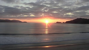 Un coucher de soleil sur une étendue d’eau calme, avec une terre ferme visible au loin.