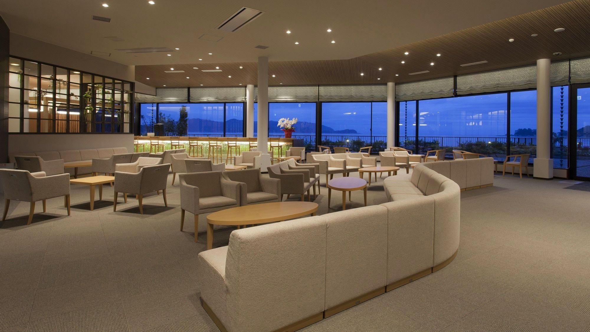 A modern lounge area with seating and a bar, large windows with a view, and a patterned carpet.