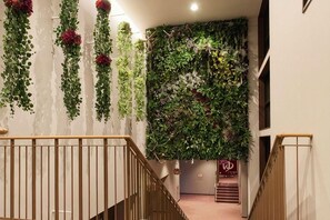 A staircase with a wooden handrail and a wall adorned with vertical green vines and red flowers. - Sanriku Hana Hotel Hamagiku (Otsuchi-cho)