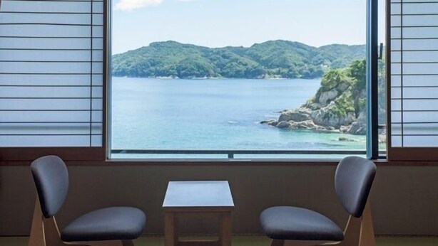 Une pièce avec deux chaises et une petite table, ainsi qu’une grande fenêtre donnant sur un paysage côtier.