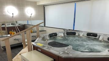 A hot tub in a room with tiled walls, a wooden bench, and a mirror.