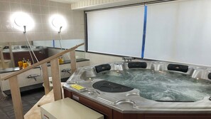 Una banyera d'hidromassatge en una habitació amb parets de rajola, una cadira de fusta i un mirall.