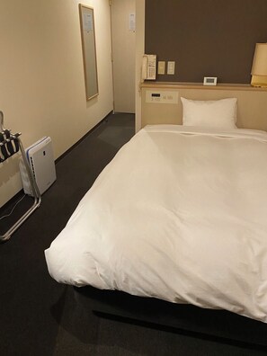 Habitació d'hotel amb un llit gran, un telèfon al costat del llit, un termòstat fixat a la paret i una làmpada de nit.