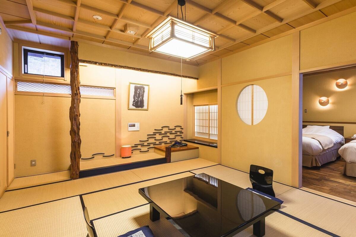 Una habitación japonesa tradicional con suelo de tatami, una mesa baja, una cama con ropa de cama estilo futón y una puerta corredera.