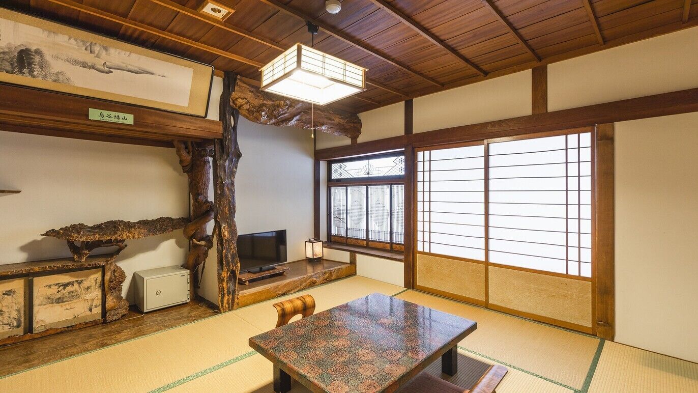 A traditional Japanese room with tatami flooring, a low wooden table, a television, and a large shoji screen window.