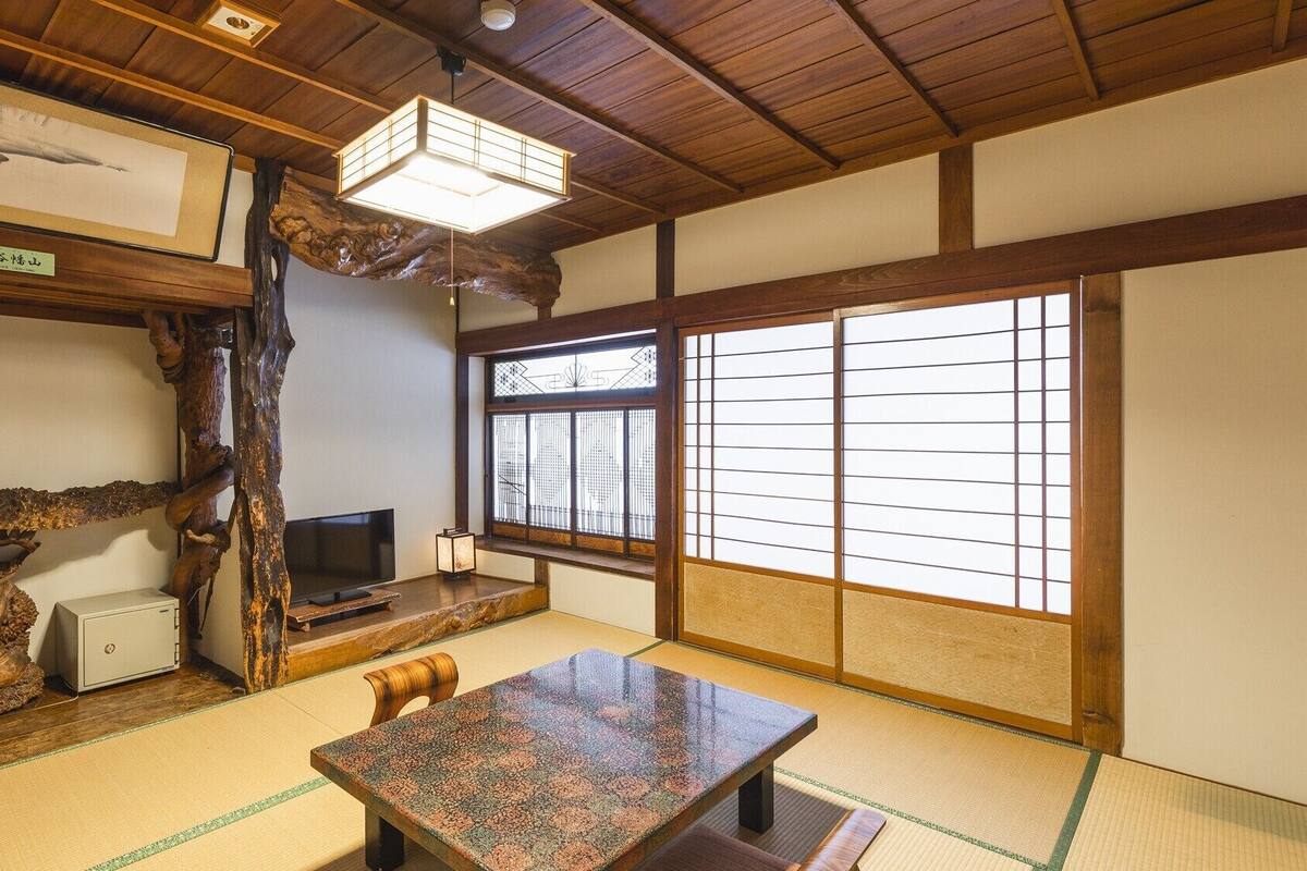 Una habitación japonesa tradicional con suelo de tatami, una mesa baja, un televisor y un ventanal con celosías shoji.