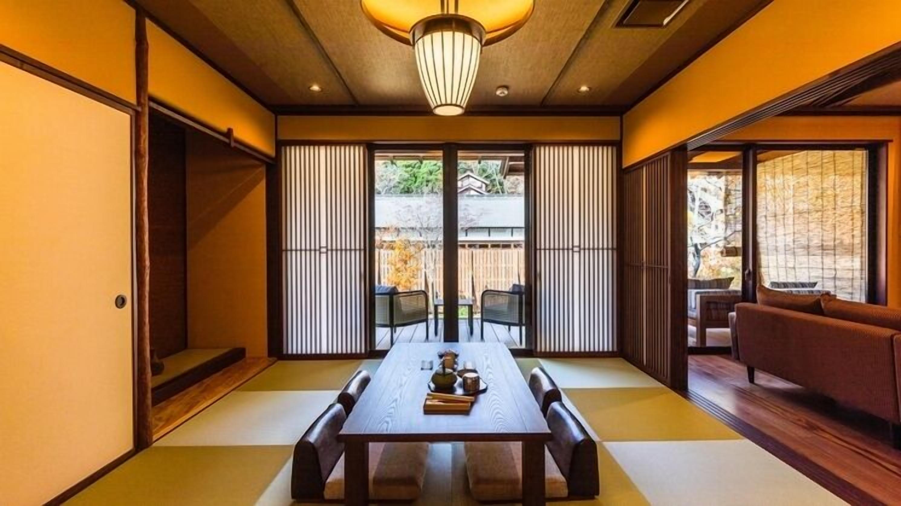 A traditional Japanese-style room with tatami flooring, a low table with cushions, sliding shoji doors, and a view of the outdoors.