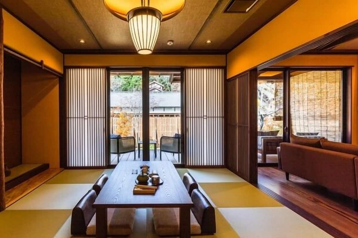 Una habitación tradicional japonesa con suelo de tatami, una mesa baja con cojines, puertas correderas shoji y vistas al exterior.