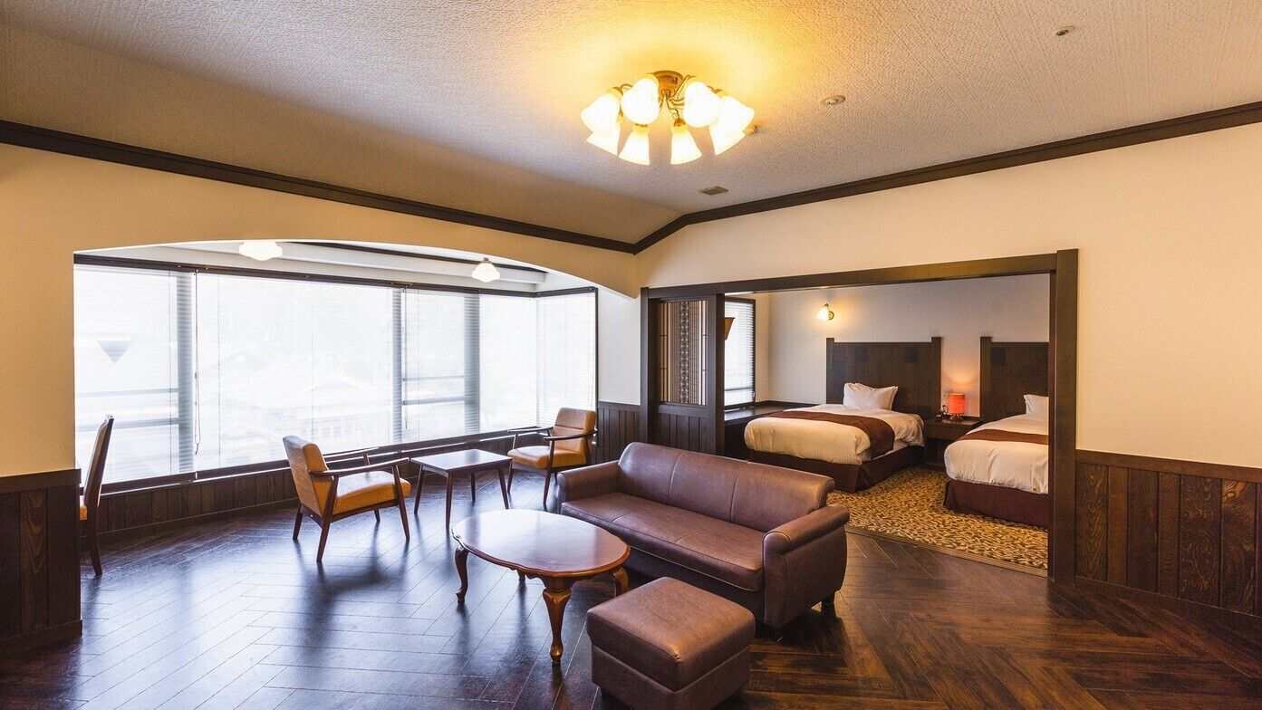 A hotel room with a large window, a sofa, a table, and two beds.