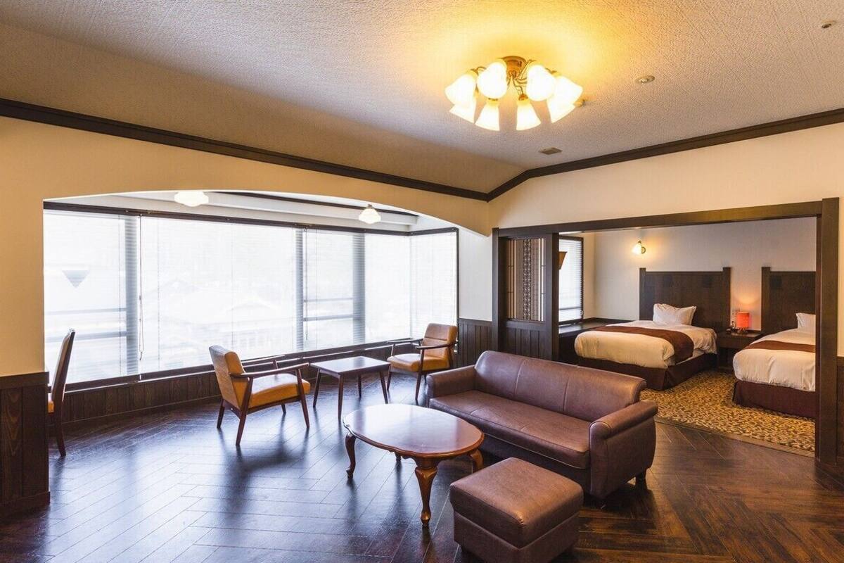 Una habitación de hotel con un ventanal grande, un sofá, una mesa y dos camas.