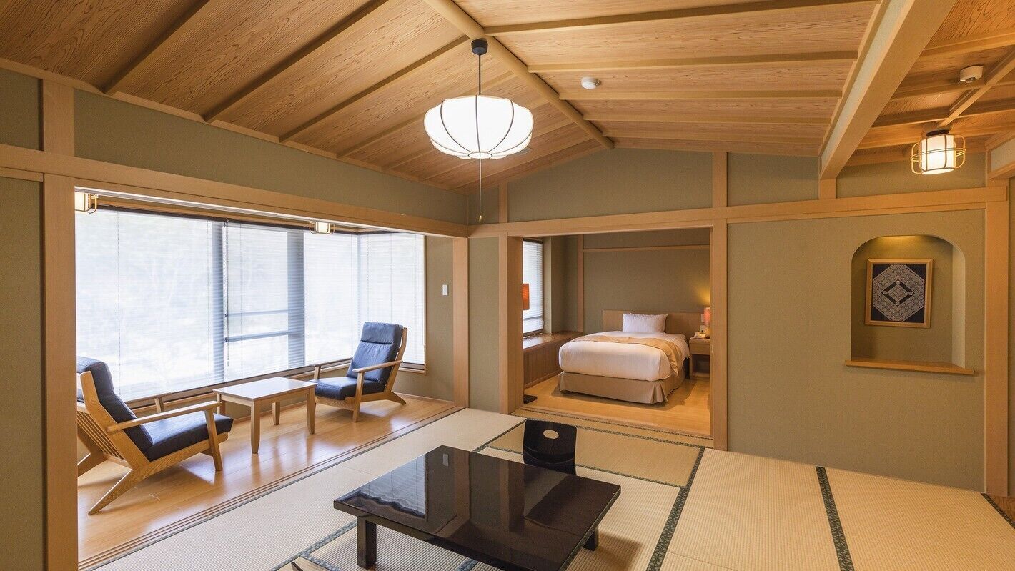 A traditional Japanese-style room with tatami flooring, a low bed, a desk, and a chair.