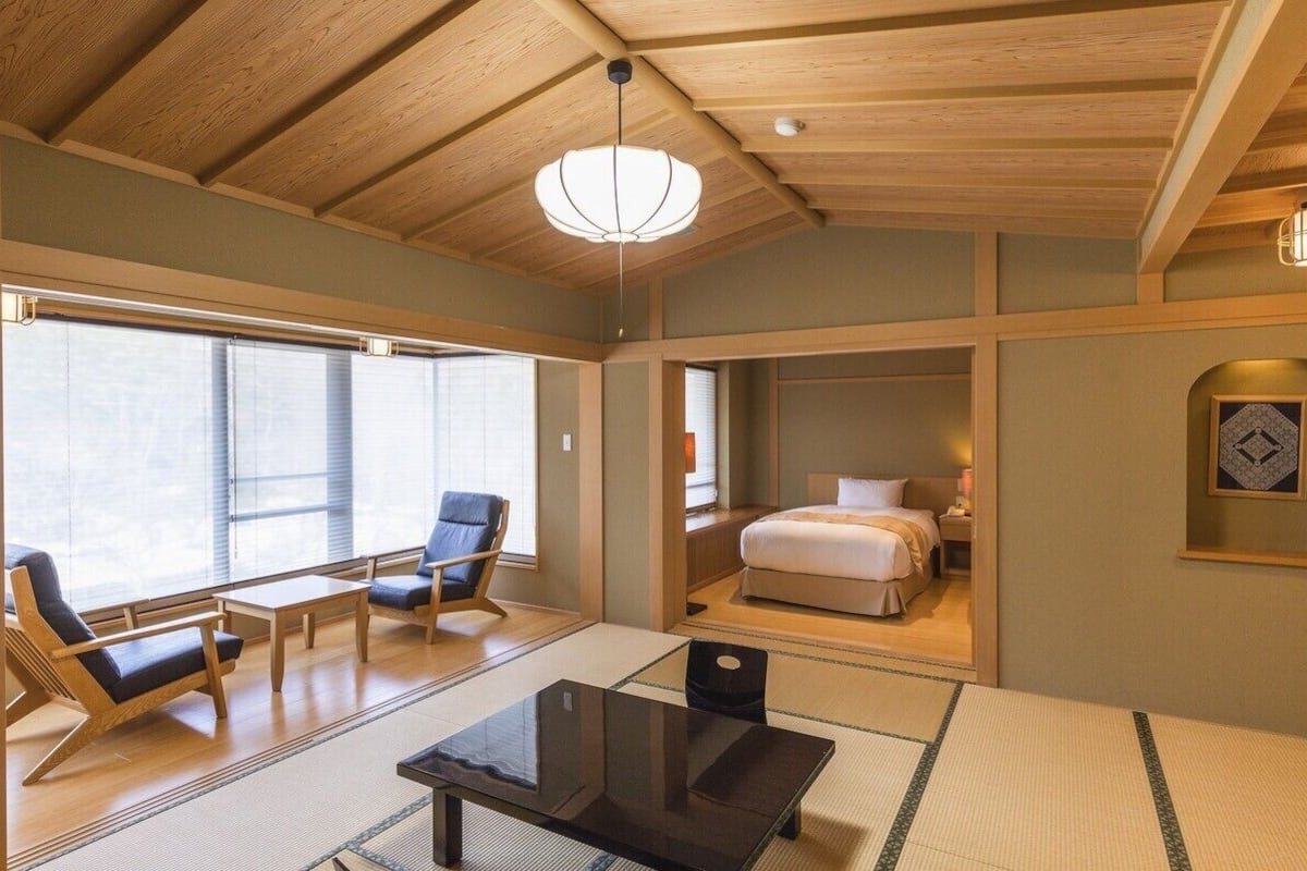 A traditional Japanese-style room with tatami flooring, a low bed, a desk, and a chair.
