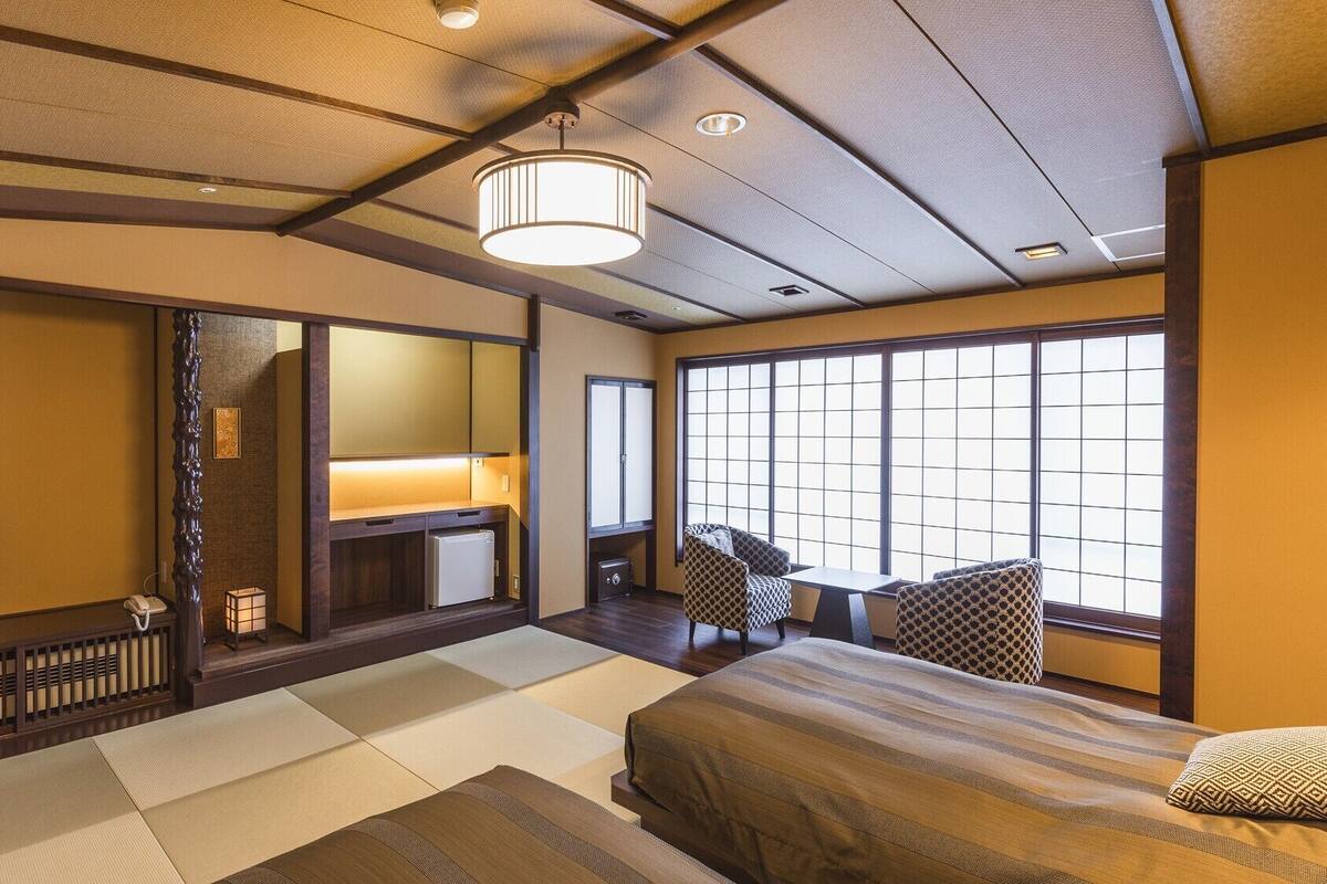 Una habitación japonesa tradicional con suelo de tatami, una cama, un televisor y una puerta corredera.