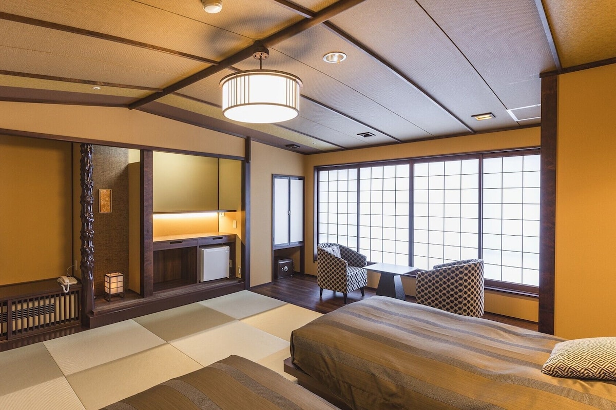 A traditional Japanese-style room with tatami flooring, a bed, a television, and a sliding door.