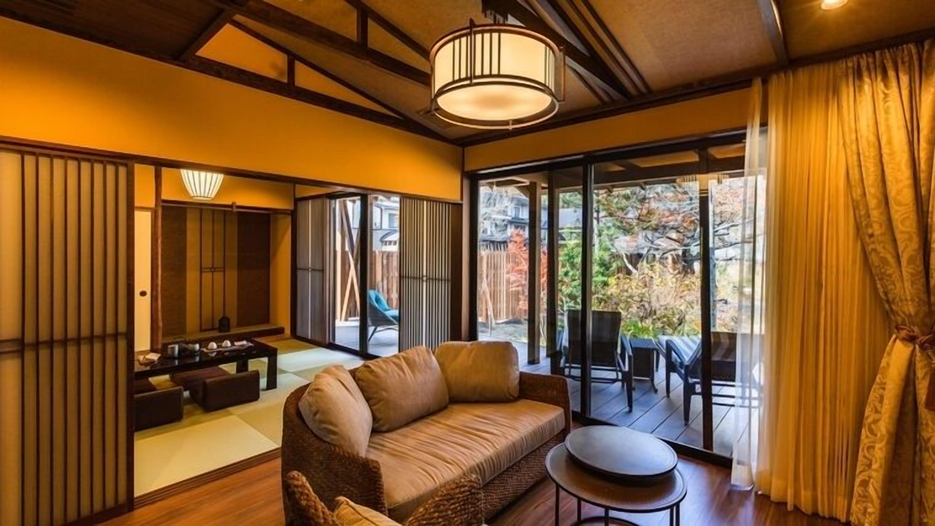 A traditional Japanese-style room with tatami flooring, a low wooden ceiling, sliding doors, and a view of a garden.