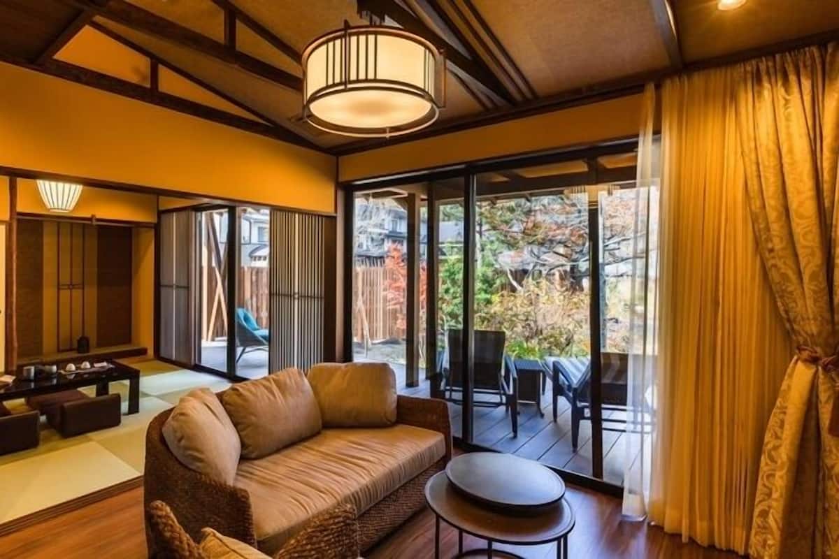 Una habitación tradicional japonesa con suelo de tatami, techo bajo de madera, puertas correderas y vista a un jardín.