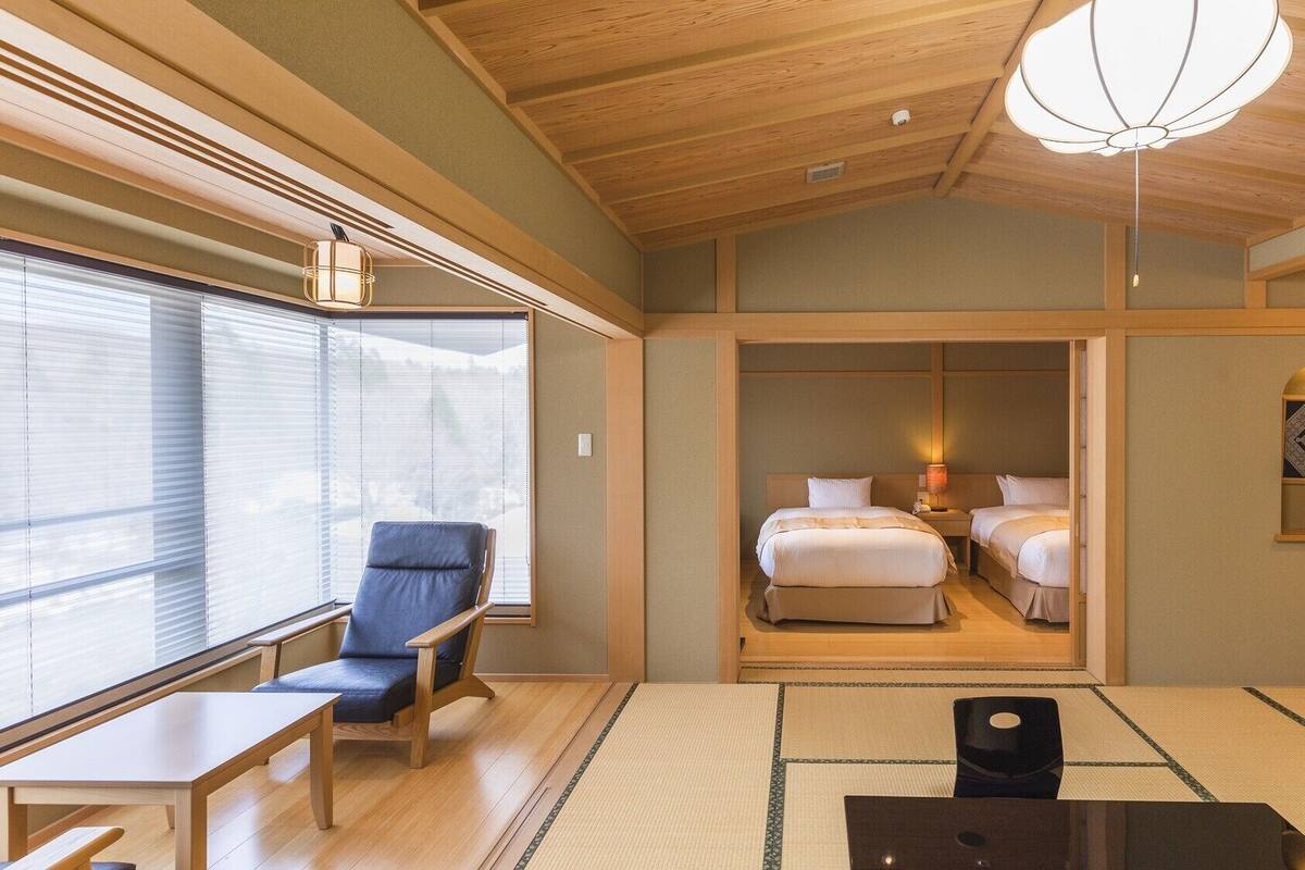 Una habitación de hotel con un ventanal grande, techo de madera, una cama, una mesita de noche y una silla.