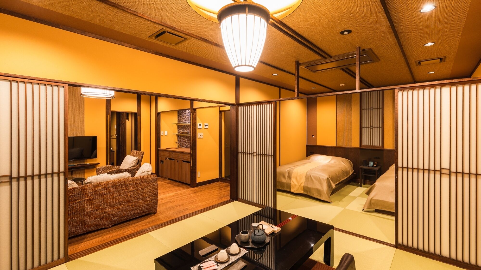 A traditional Japanese-style hotel room with tatami flooring, a low table with tea set, a bed with a futon, and sliding doors.