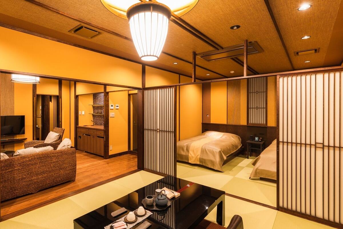 Habitación de hotel japonesa tradicional con suelo de tatami, una mesa baja con juego de té, una cama con futón y puertas correderas.