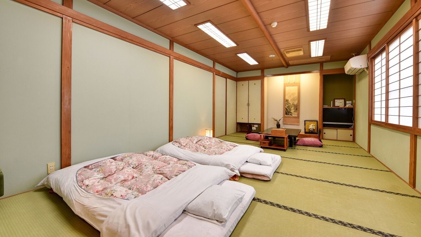 Een traditionele Japanse kamer met tatami vloeren, twee bedden met bloemenbedrukking, een futon, een houten bureau en een schuifdeur.