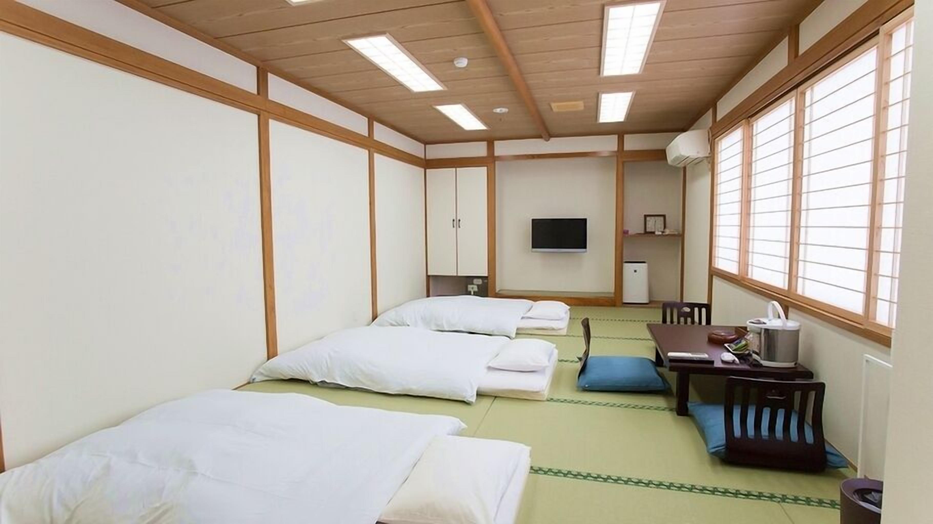 Een traditionele Japanse kamer met tatami vloerbedekking, twee bedden, een bureau en een televisie.