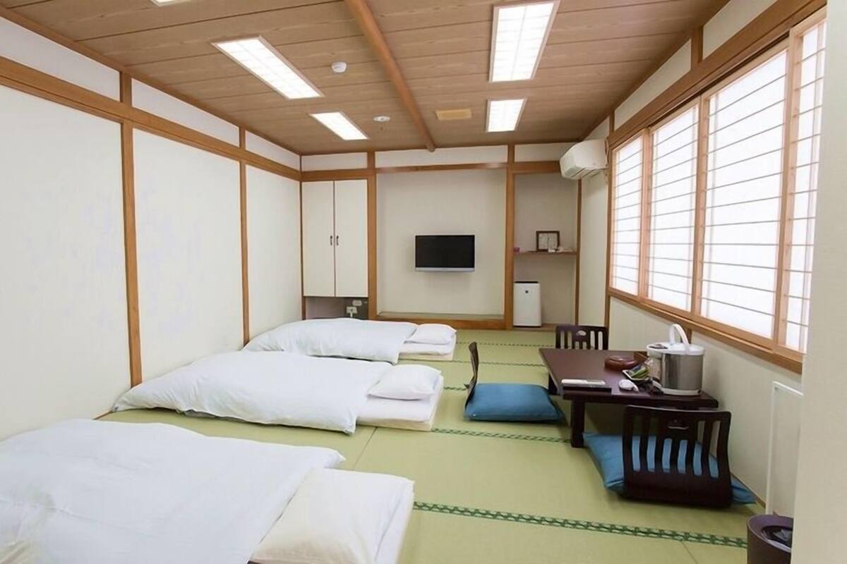 Une pièce de style japonais traditionnel, avec un sol recouvert de tatamis, deux lits, un bureau et un téléviseur.