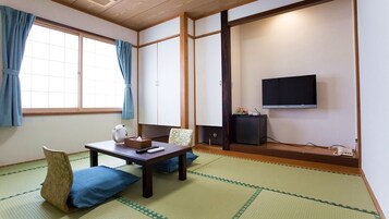 Una habitación japonesa tradicional con suelo de tatami, una mesa baja con cojines, un televisor y puertas correderas.